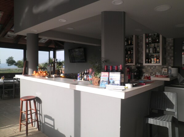 A bar area with a counter, stools, and a view of the ocean. - Haridimos Apartments (Platanias)
