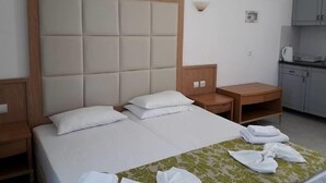 A hotel room with a large bed, a wooden nightstand, a small table, and a kitchenette area. - Haridimos Apartments (Platanias)