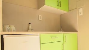 A compact kitchen with a white refrigerator, green cabinets, and a countertop with jars. - Ilaeira rooms (Zakynthos)