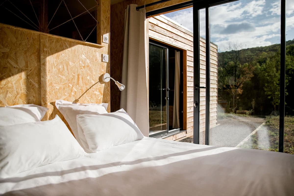 A bedroom with a large bed, a nightstand, and a window with a view of a forested area.