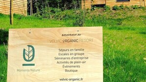 A wooden signboard for Volvic Organic Resort listing amenities like family stays, group hikes, business seminars, outdoor activities, events, and a boutique. - Volvic Organic Resort (Volvic)