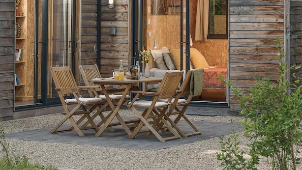 A wooden cabin with a dining area featuring a table and chairs, a small kitchen, and a bathroom with a shower. - Volvic Organic Resort (Volvic)