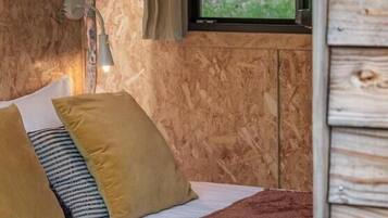 Un dormitorio con cama, almohadas, una ventana con vista a follaje y una pared de madera.
