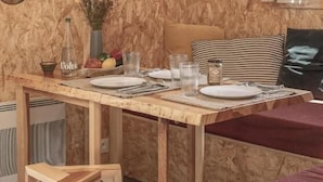 A cozy room with a wooden wall, a dining table set with plates and glasses, a bed with striped pillows, and a window with curtains. - Volvic Organic Resort (Volvic)