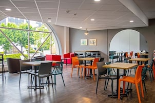 Un área de comedor moderna con mesas, sillas, ventanas amplias y vistas a la vegetación exterior.