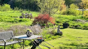 Un espace extérieur verdoyant, avec une table de pique-nique et des chaises, entouré d’arbres et d’un arbuste rouge.