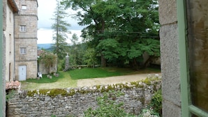 Un bâtiment en pierre doté d’une tour, un jardin avec un mur en pierre et une vue sur les arbres.