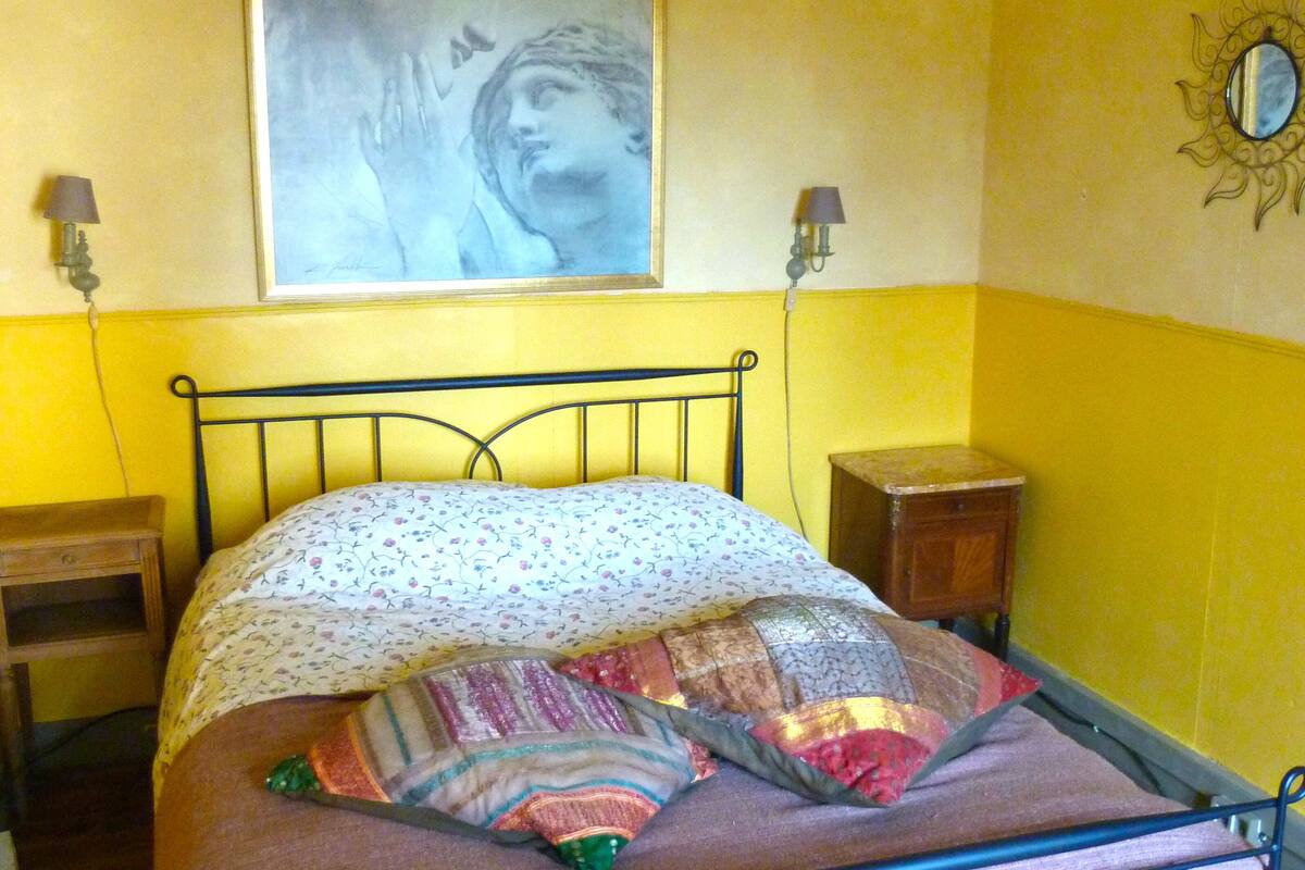 Ein Schlafzimmer mit einem Bett, einem Nachttisch, einer Wandlampe und einem Gemälde.