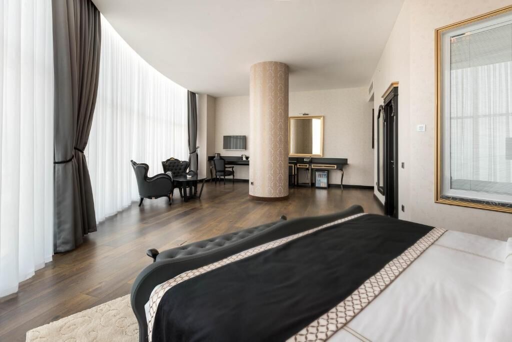 A hotel room with a large bed, a desk, a chair, a mirror, and a large window with curtains.