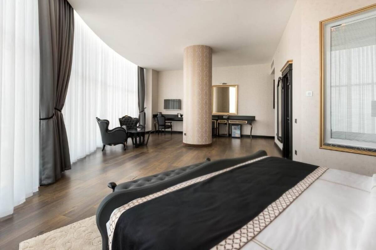 A hotel room with a large bed, a desk, a chair, a mirror, and a large window with curtains.