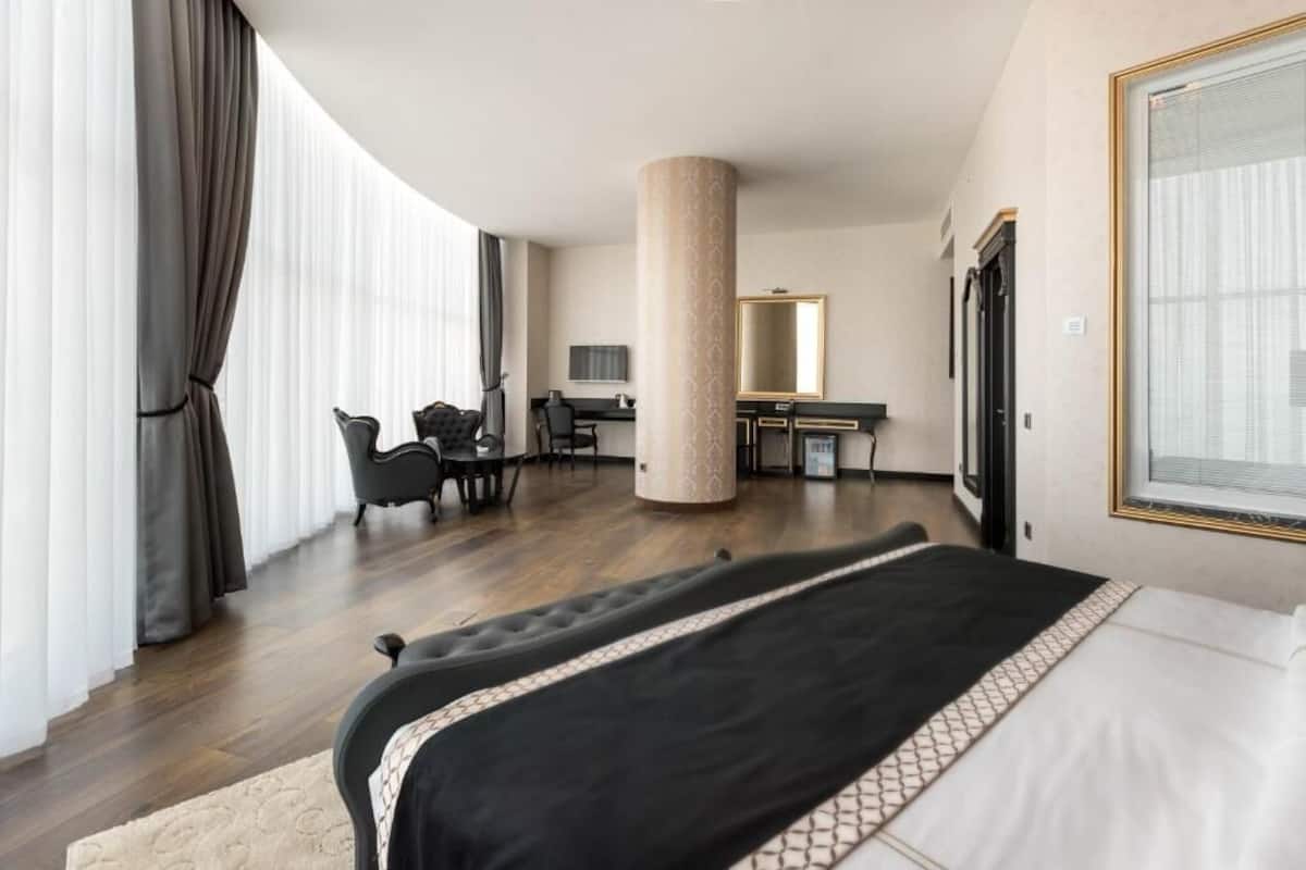 A hotel room with a large bed, a desk, a chair, a mirror, and a large window with curtains.