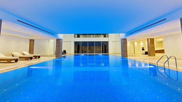 Una amplia piscina interior con sillas de descanso, vista despejada del interior y un diseño arquitectónico moderno.