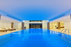 A large indoor swimming pool with lounge chairs, a clear view of the interior, and a modern architectural design. - JRW Welmond Hotel (Batumi)