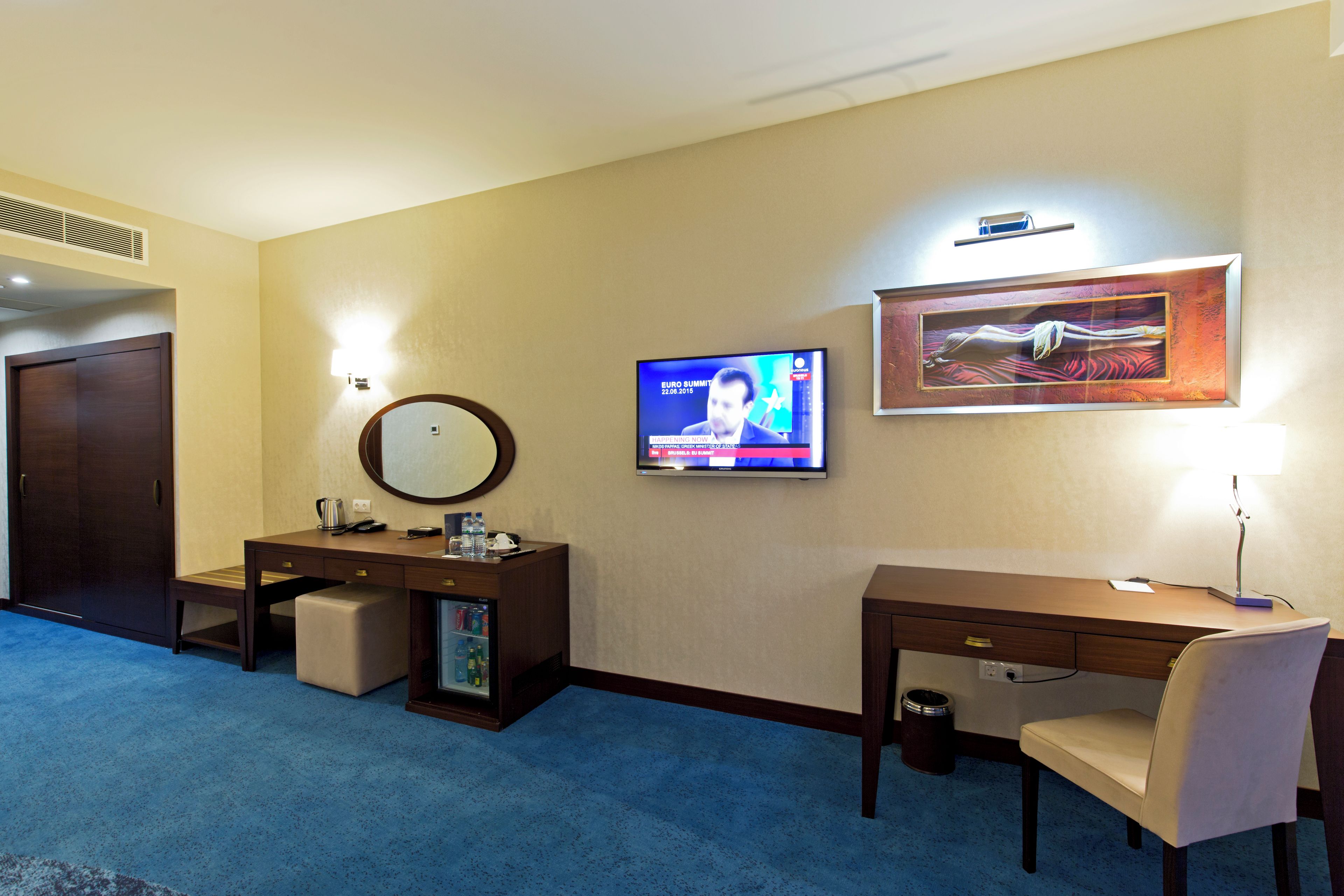 A hotel room with a desk, chair, television, and a framed artwork on the wall.