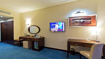 A hotel room with a desk, chair, television, and a framed artwork on the wall.