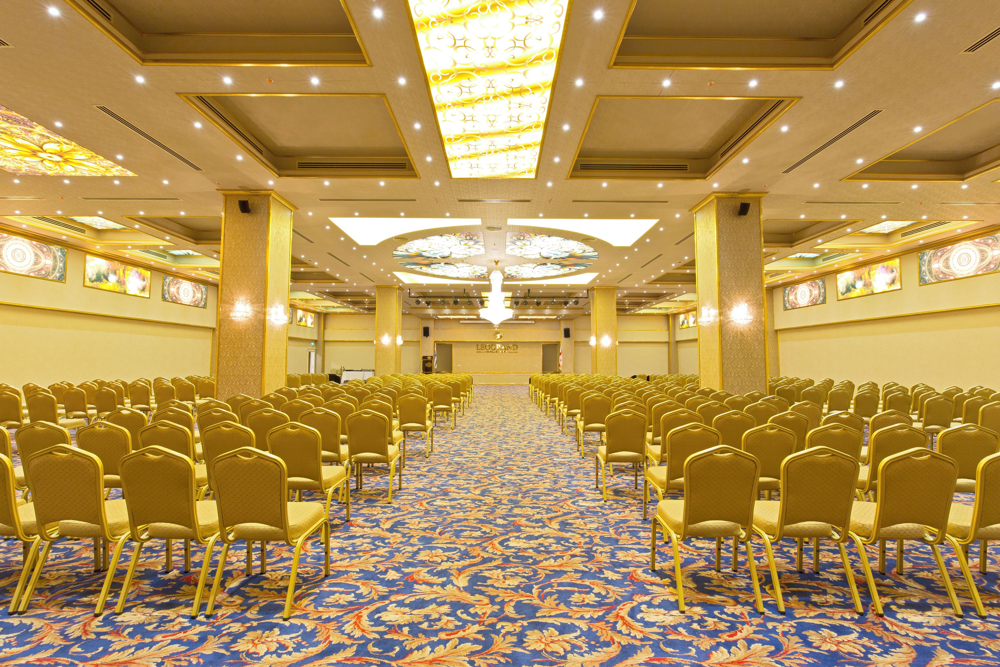 A conference room with rows of chairs, a patterned carpet, and a chandelier.