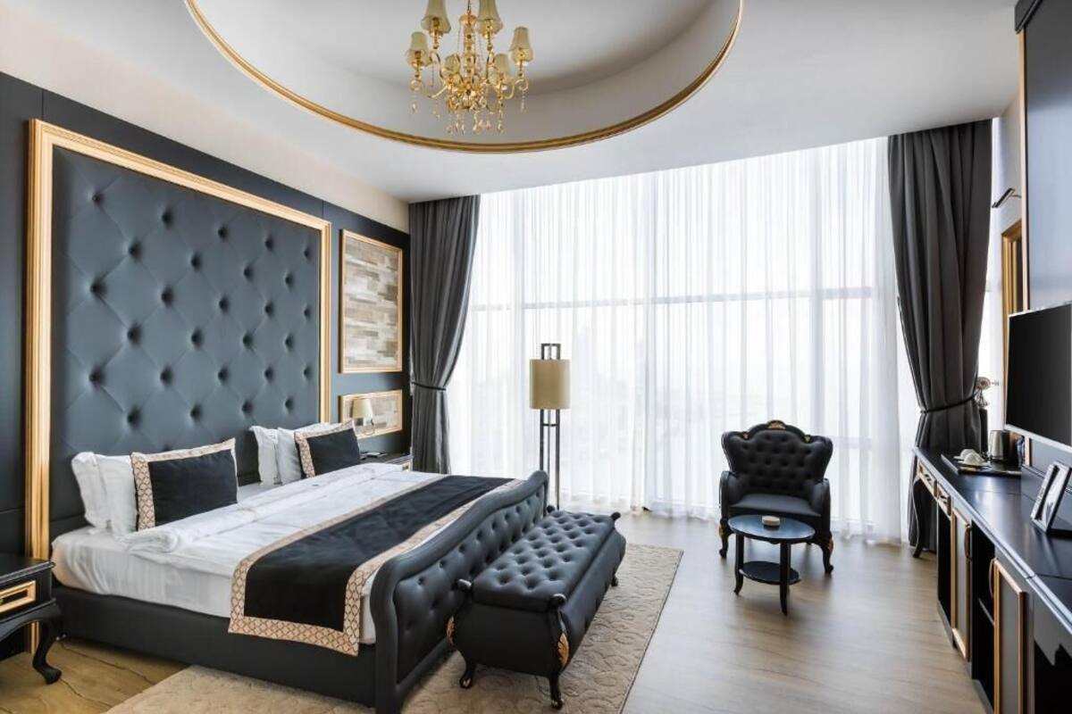 A modern bedroom with a large bed, a bench, a chair, and a TV.