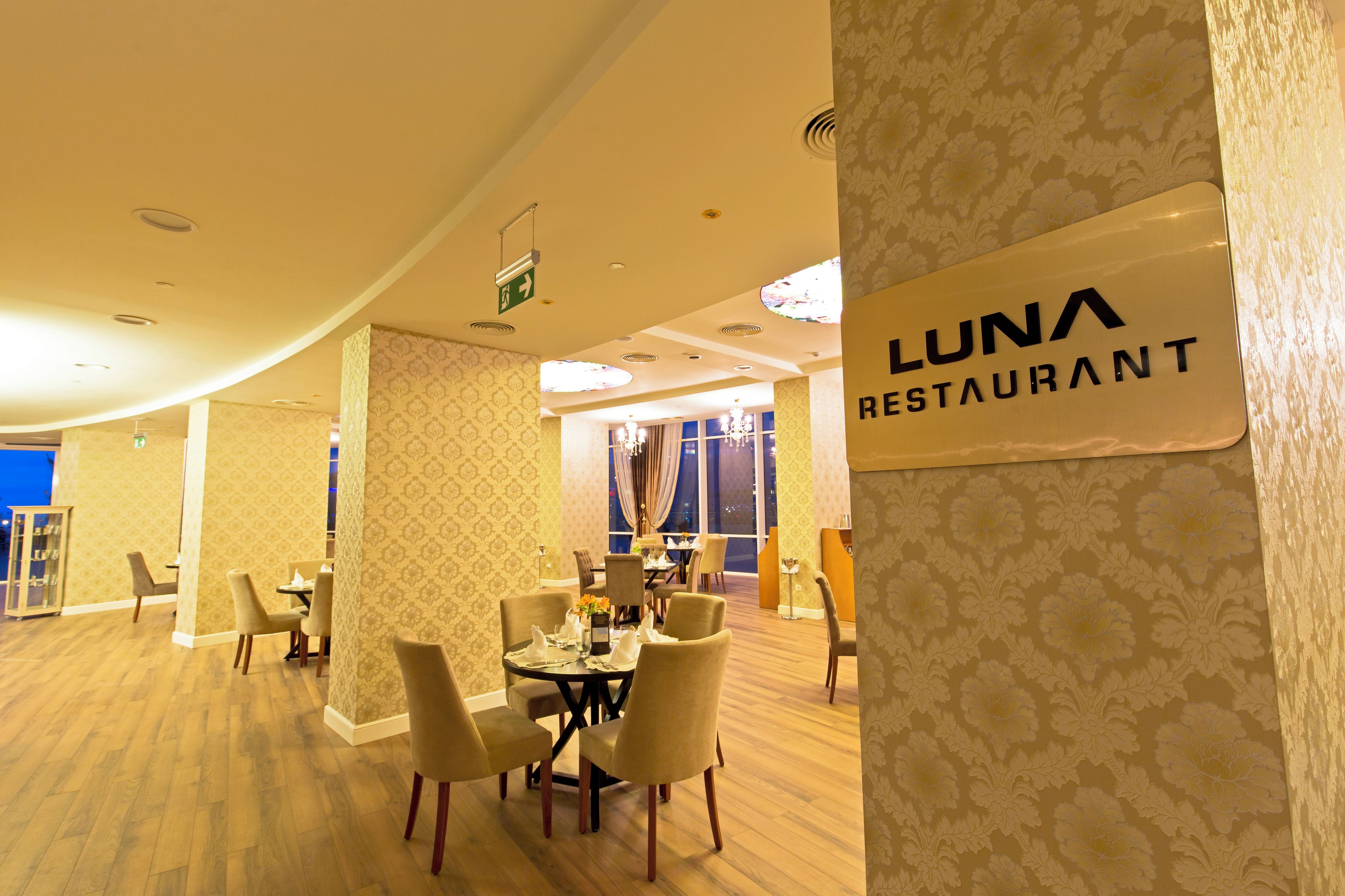 A restaurant interior with a sign reading 'LUNA RESTAURANT,' tables with chairs, and a patterned wall.