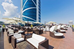 A rooftop lounge with wicker furniture, outdoor umbrellas, and a view of a modern building. - JRW Welmond Hotel (Batumi)