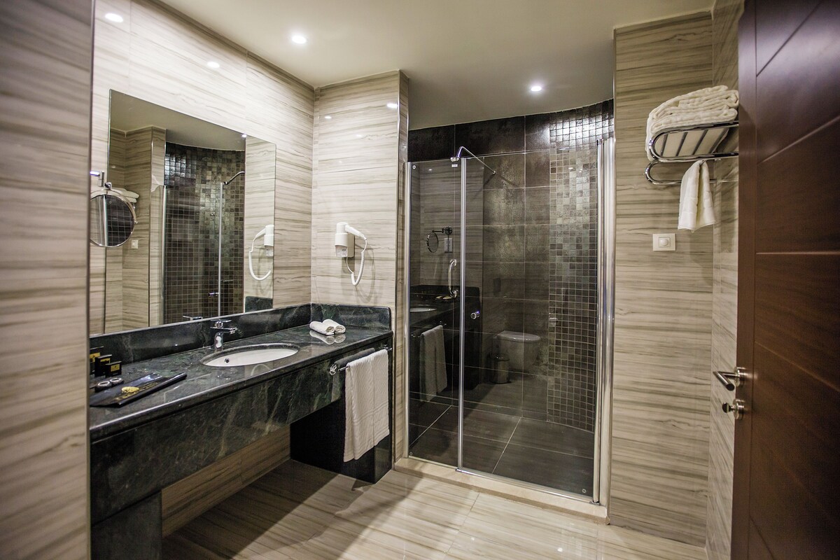 A modern bathroom with a glass-enclosed shower, a large mirror, and a marble countertop.