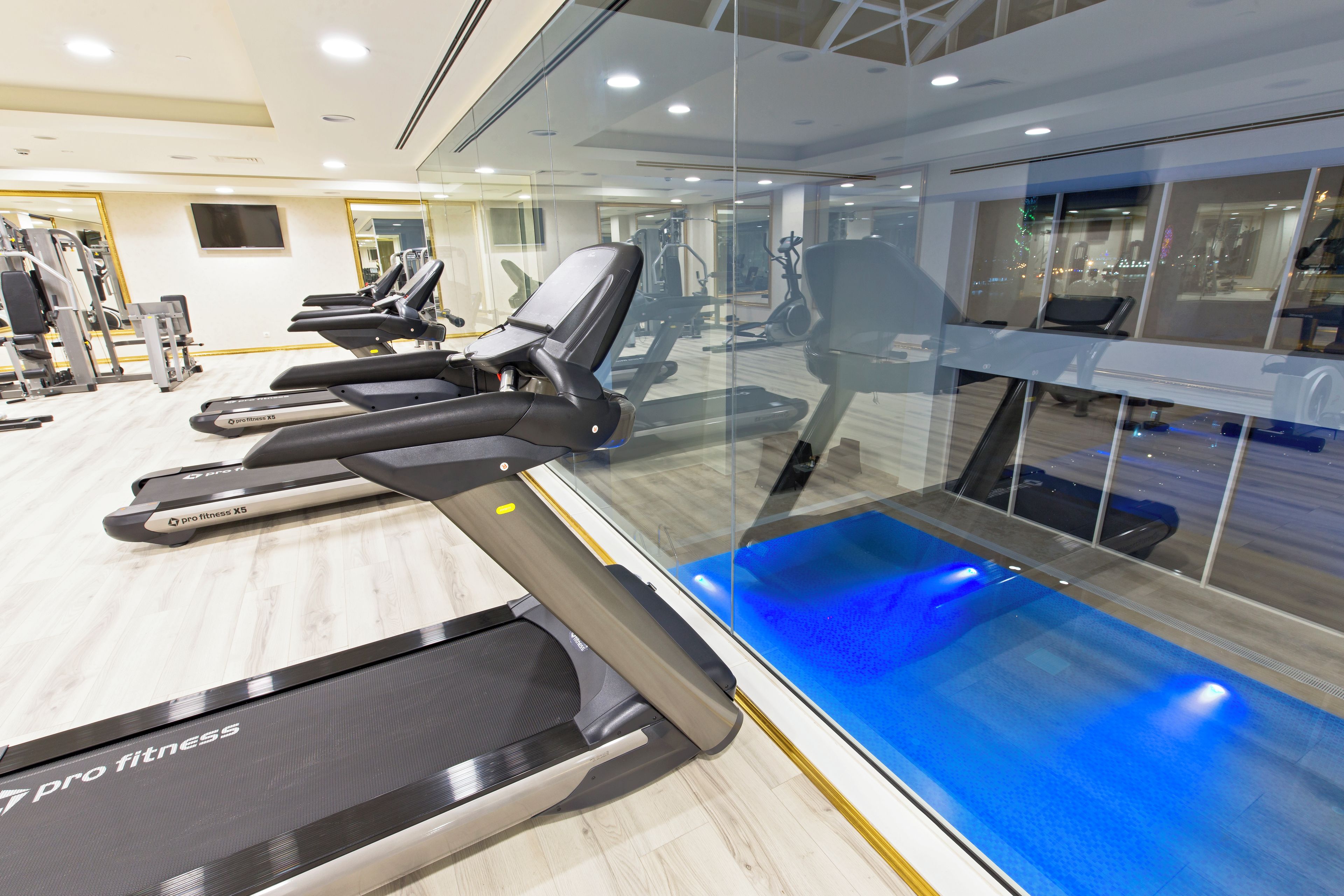A gym with treadmills, exercise bikes, and a blue-lit pool area.