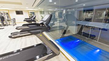 A gym with treadmills, exercise bikes, and a blue-lit pool area.