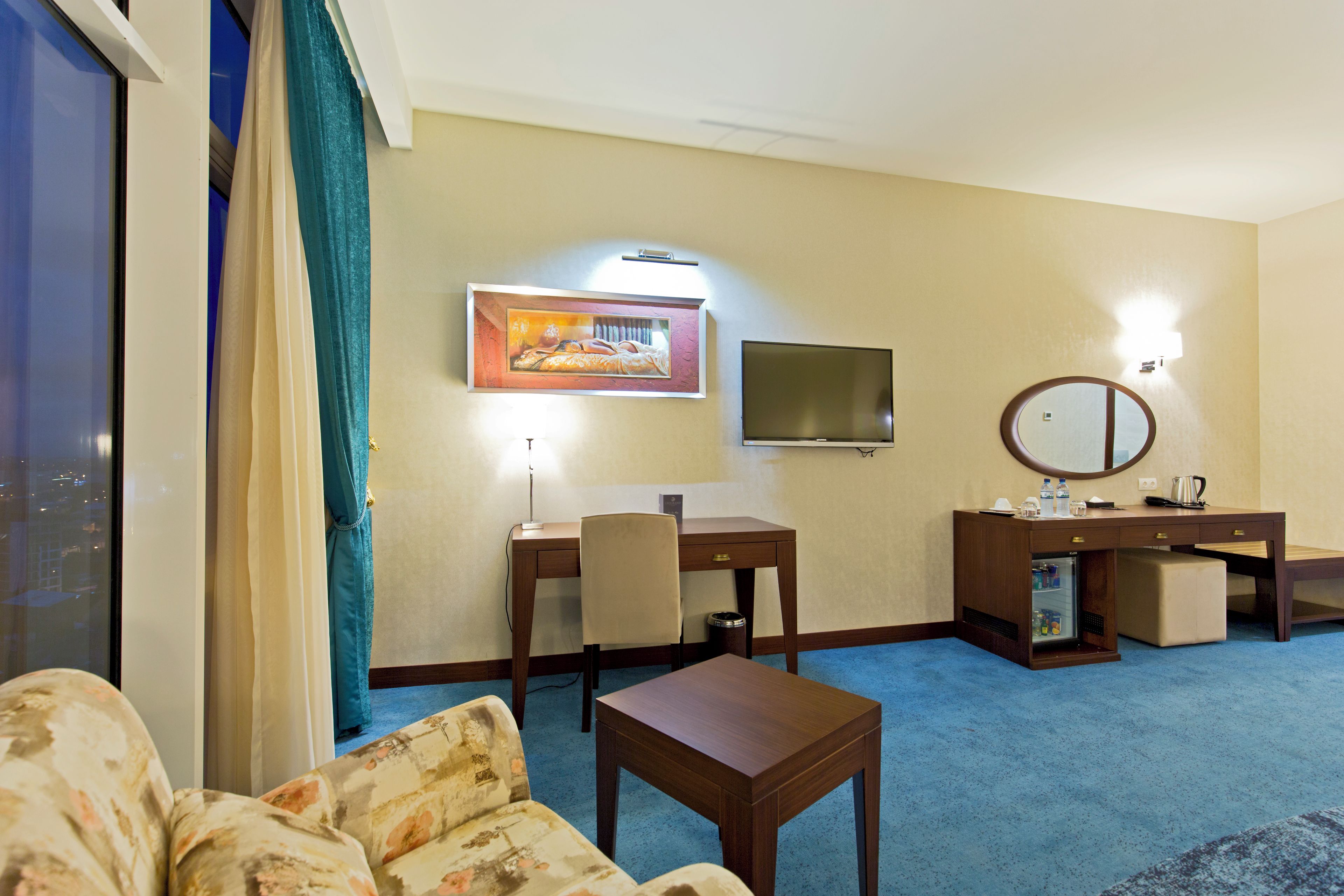 Ein Hotelzimmer mit Sofa, Schreibtisch, Fernseher, Spiegel und einem Bild an der Wand.