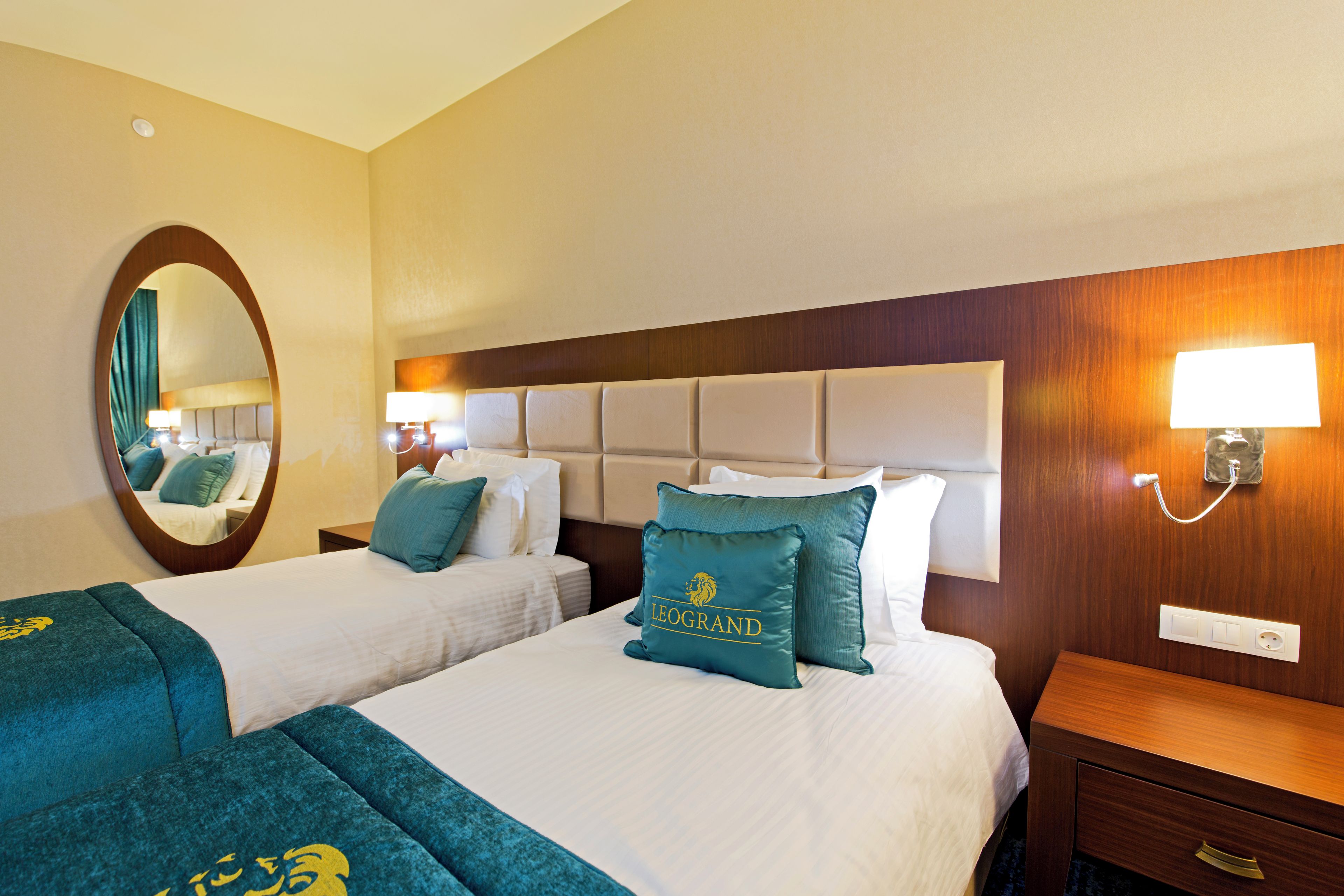 A hotel room with two beds, a large mirror, a headboard with a light, and a bedside table with a lamp.
