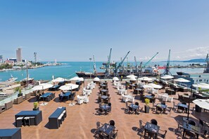 A rooftop terrace with outdoor seating and a view of the harbor. - JRW Welmond Hotel (Batumi)