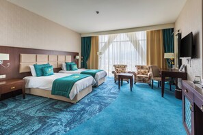 A hotel room with two beds, a TV, a desk, and a chair. - JRW Welmond Hotel (Batumi)
