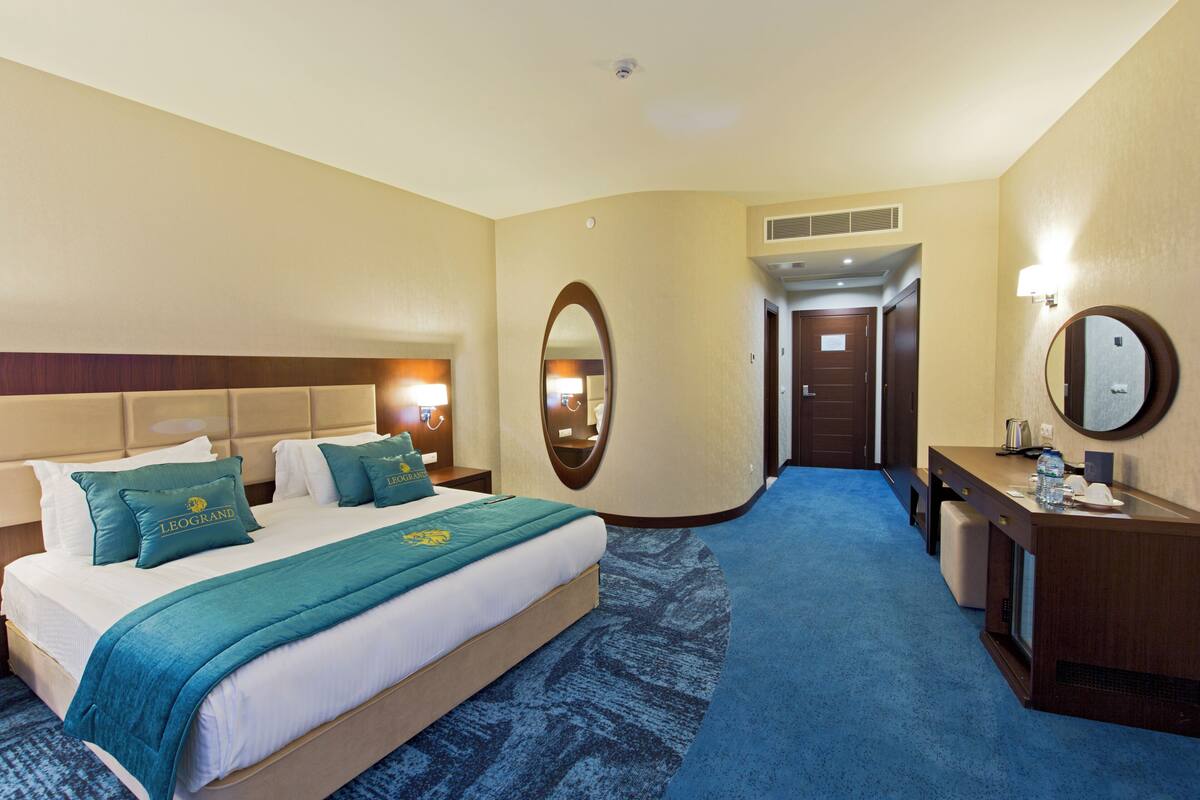 A hotel room with a bed, a desk, a mirror, and a door leading to another room.