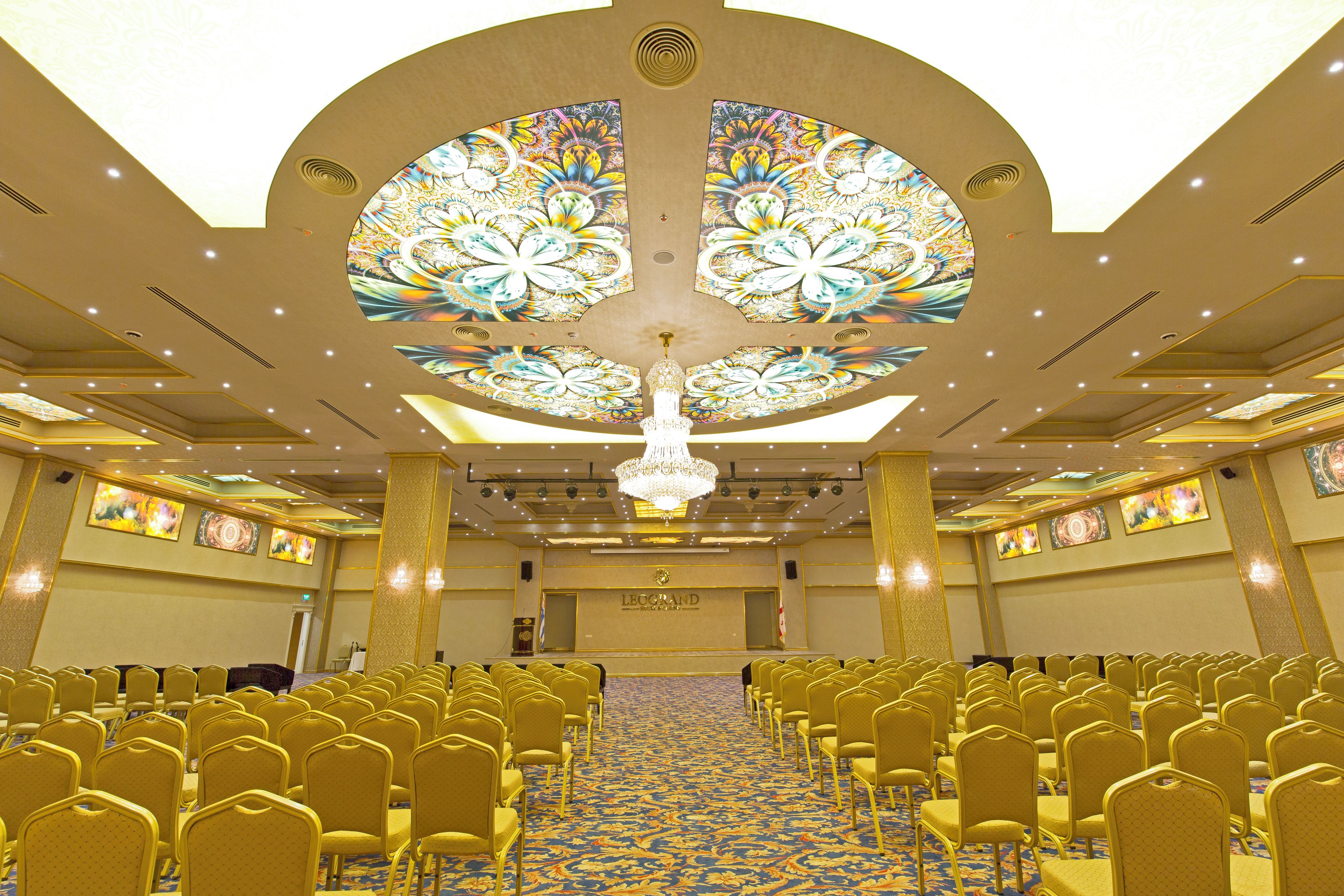 A conference room with rows of chairs, a chandelier, and a patterned ceiling.