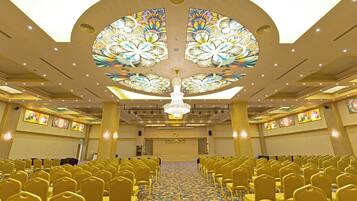 A conference room with rows of chairs, a chandelier, and a patterned ceiling.