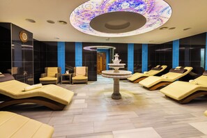 A spa room with multiple sun loungers, a central fountain, and a patterned ceiling. - JRW Welmond Hotel (Batumi)