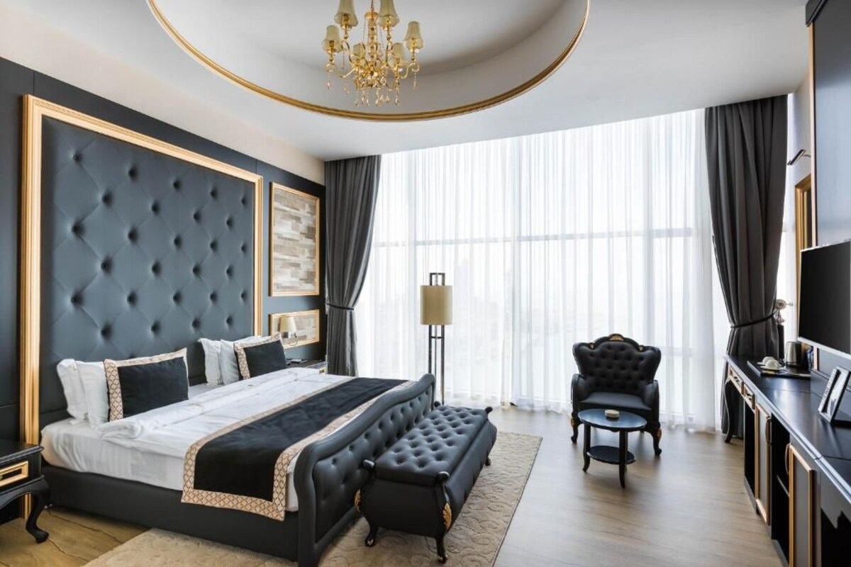 A modern bedroom with a large bed, a bench, a chair, and a TV.