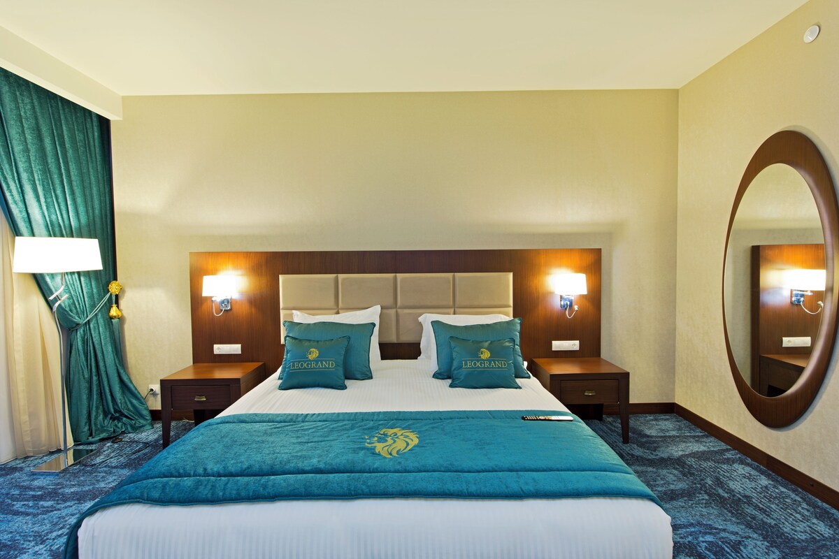 A hotel room with a large bed, two bedside tables, a mirror, and a view of the room.