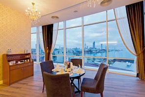 A dining room with a table set for four, a chandelier, and a view of a cityscape through large windows. - JRW Welmond Hotel (Batumi)