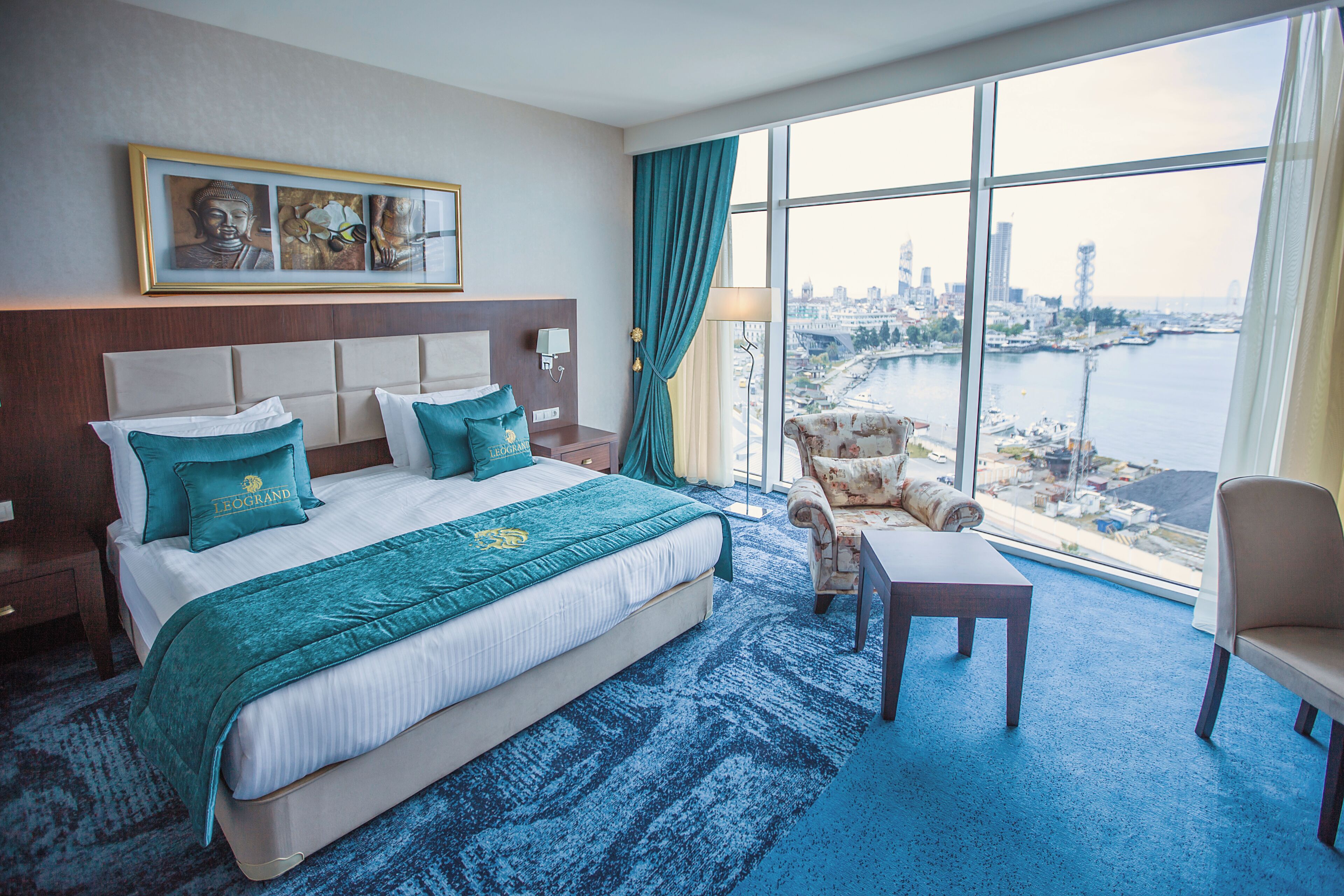 A hotel room with a large bed, a view of the cityscape, a city skyline, and a body of water.