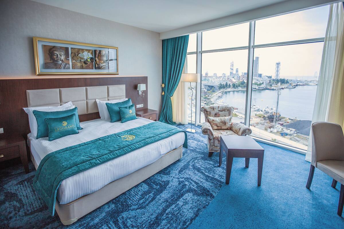 A hotel room with a large bed, a view of the cityscape, a city skyline, and a body of water.