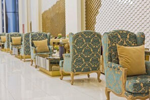 A row of ornate armchairs with patterned upholstery and gold accents, arranged in a well-lit, tiled room with a decorative wall in the background. - JRW Welmond Hotel (Batumi)