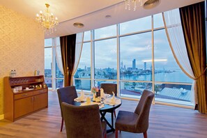 Een eetkamer met een tafel voor vier personen, een kroonluchter en een uitzicht op een stadsbeeld door grote ramen.