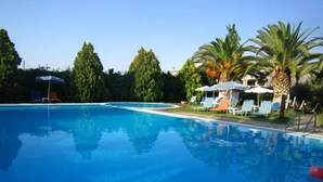 A clear swimming pool with lounge chairs and umbrellas, surrounded by palm trees and greenery. - Imperial Studios (Malevizi)