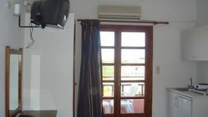 A small, clean room with a wooden door, a window with curtains, a small table, and a white cabinet. - Imperial Studios (Malevizi)