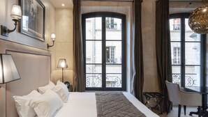 A hotel room with a large bed, a desk, and a view of the city through a large window. - Hotel Le Presbytère (Paris)