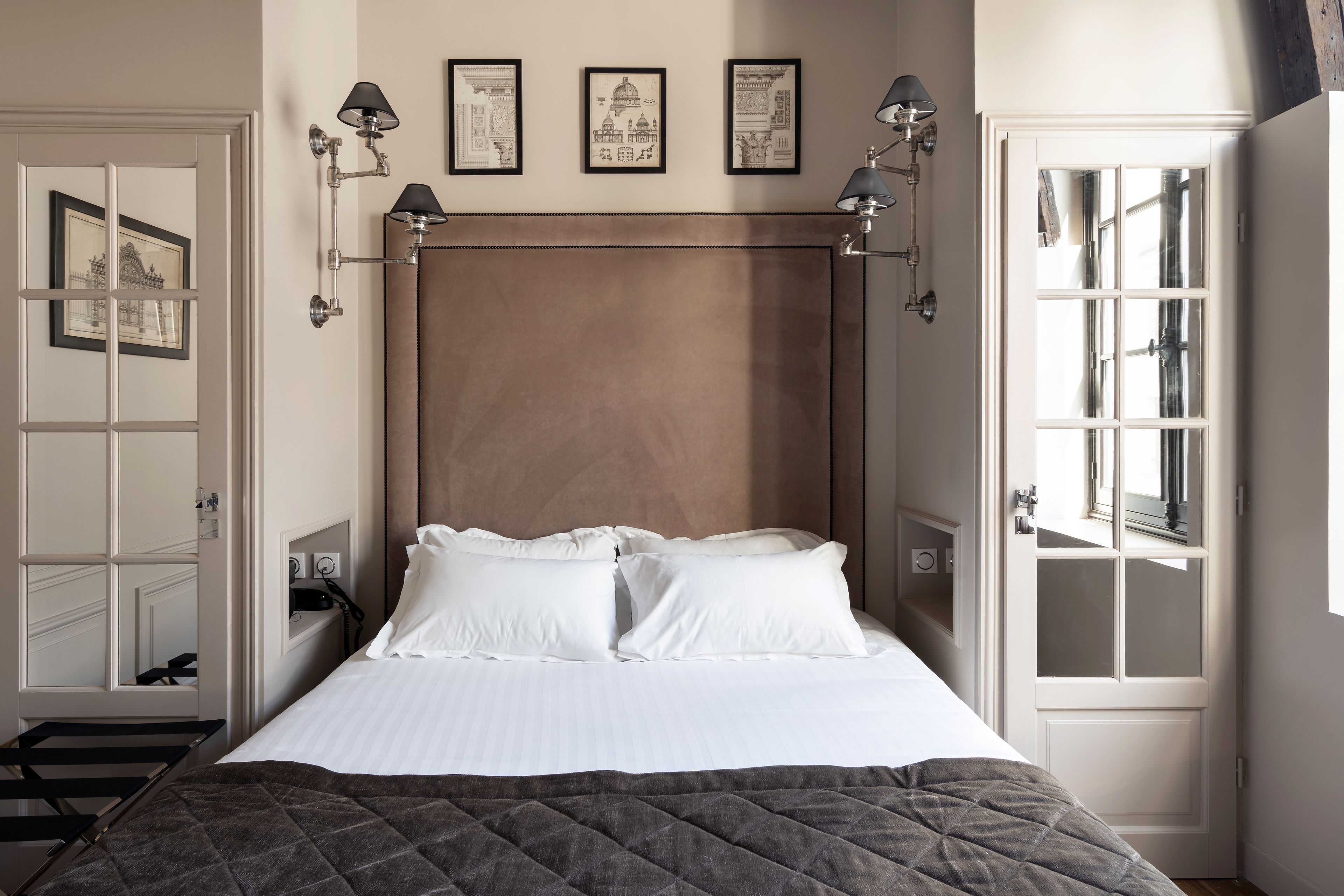 A neatly arranged bedroom with a bed, bedside lamps, and framed pictures on the wall.