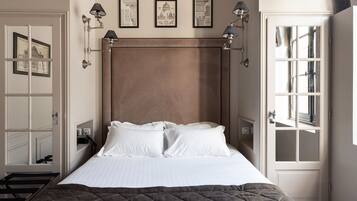 A neatly arranged bedroom with a bed, bedside lamps, and framed pictures on the wall.