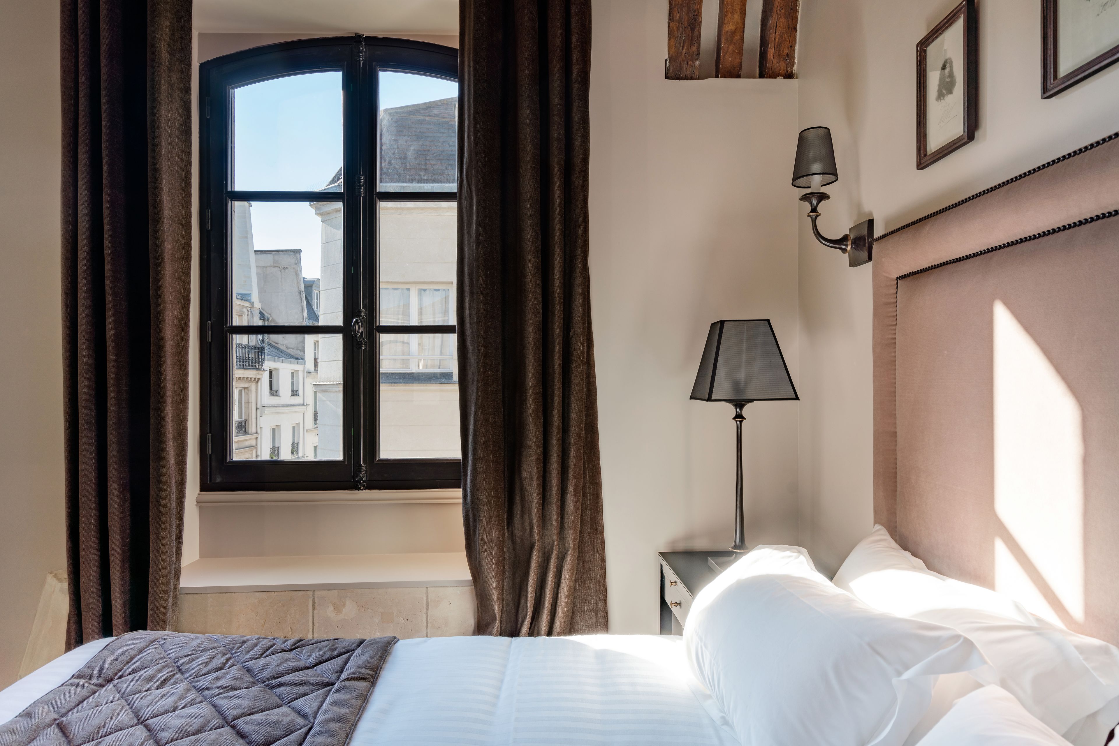 A hotel room with a bed, a nightstand, a lamp, and a window with curtains.