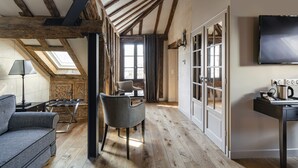 A room with exposed wooden beams, a sofa, a chair, a table, and a TV. - Hotel Le Presbytère (Paris)