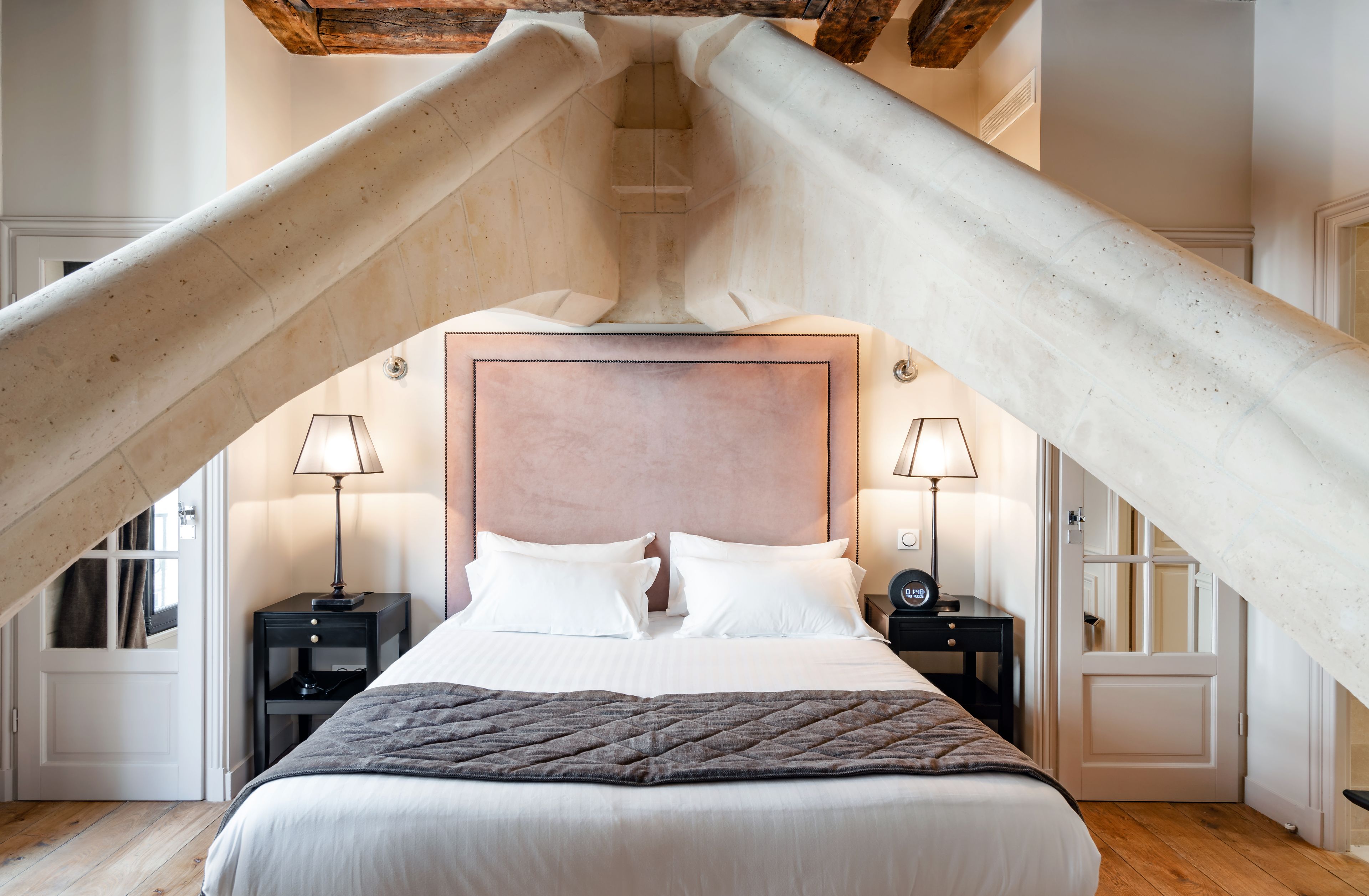 Un dormitorio con una cama grande, dos mesitas de noche con lámparas y una estructura de vigas en el techo de madera.
