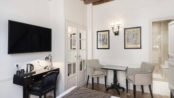 Habitación de hotel con cama, escritorio y silla, una mesa con dos sillas, televisión y obras de arte en las paredes.